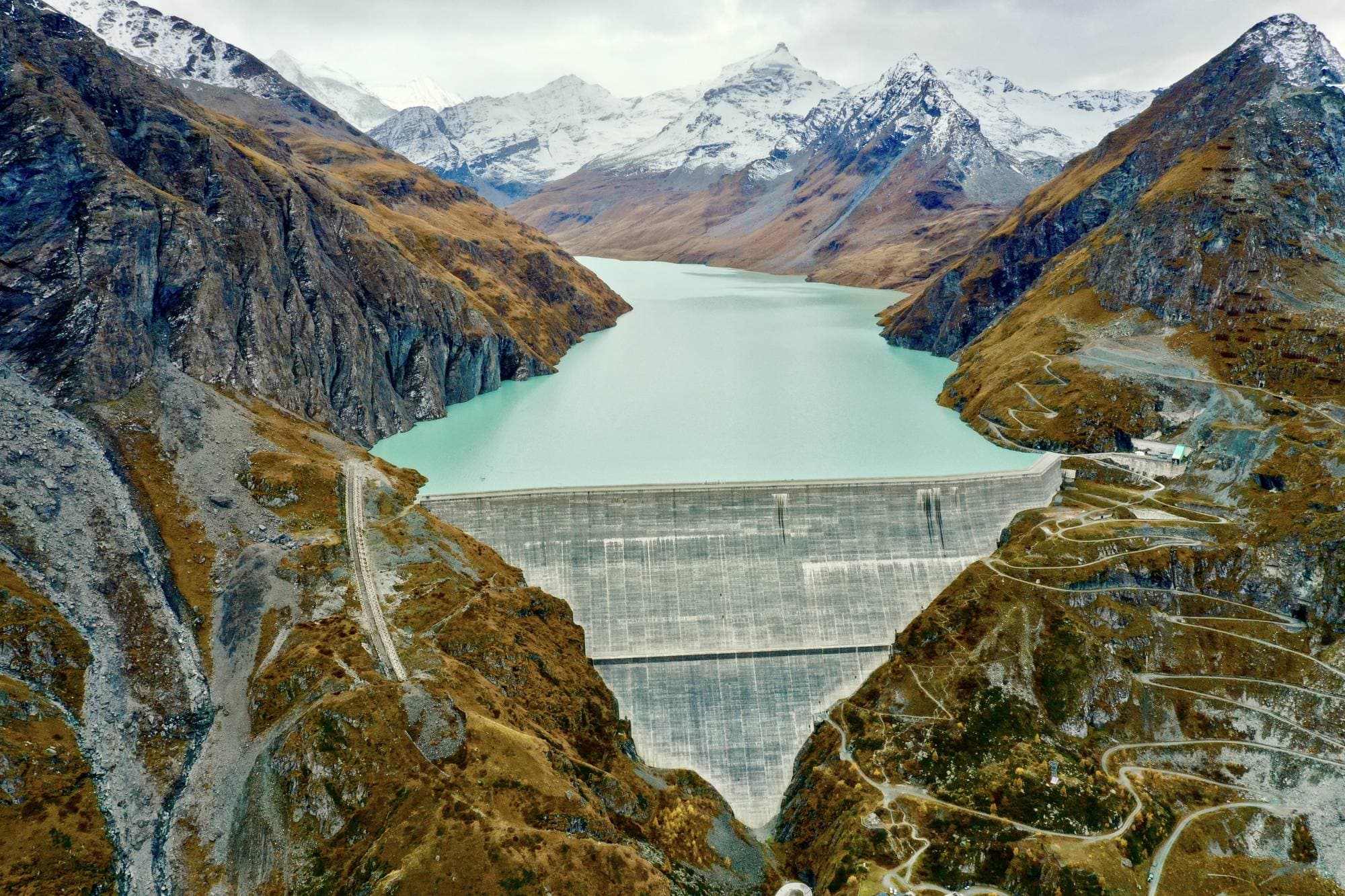 Aerial view of a concrete gravity dam and its reservoir in the Alps
